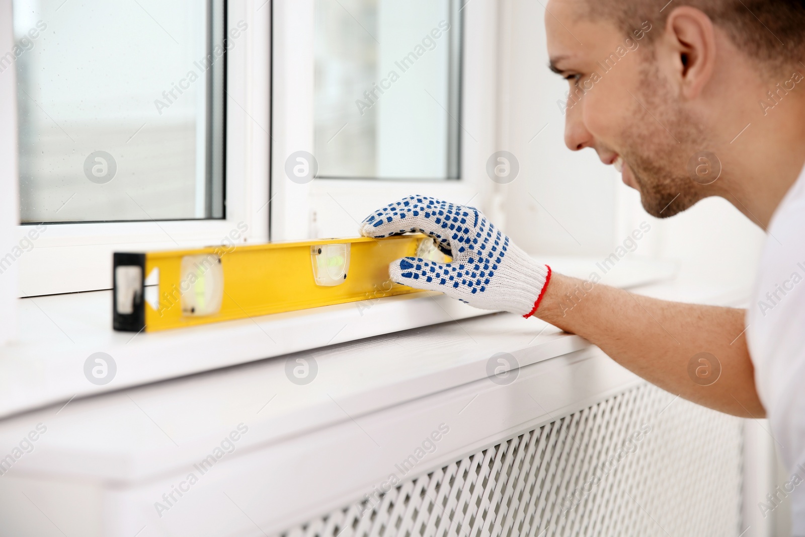 Photo of Construction worker using bubble level while installing window indoors, closeup