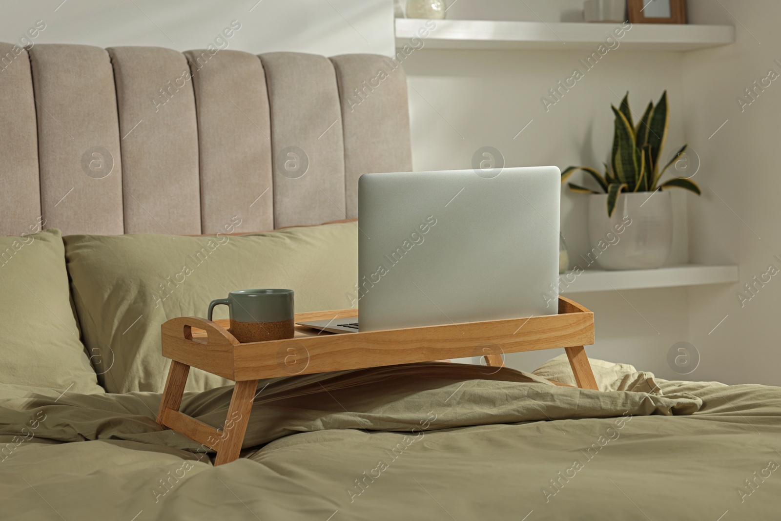 Photo of Wooden tray with modern laptop and cup of aromatic drink on bed indoors