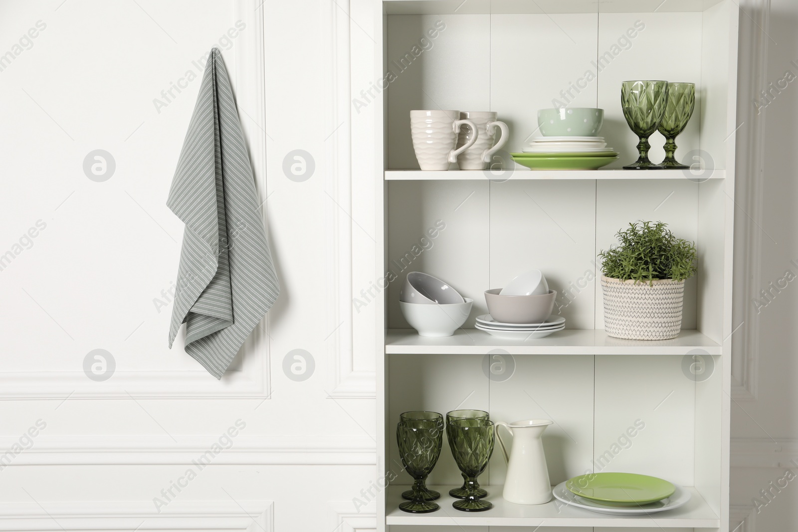 Photo of Different clean dishware and houseplant on shelves in cabinet indoors