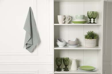 Photo of Different clean dishware and houseplant on shelves in cabinet indoors