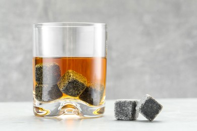 Photo of Whiskey stones and drink in glass on light table, closeup