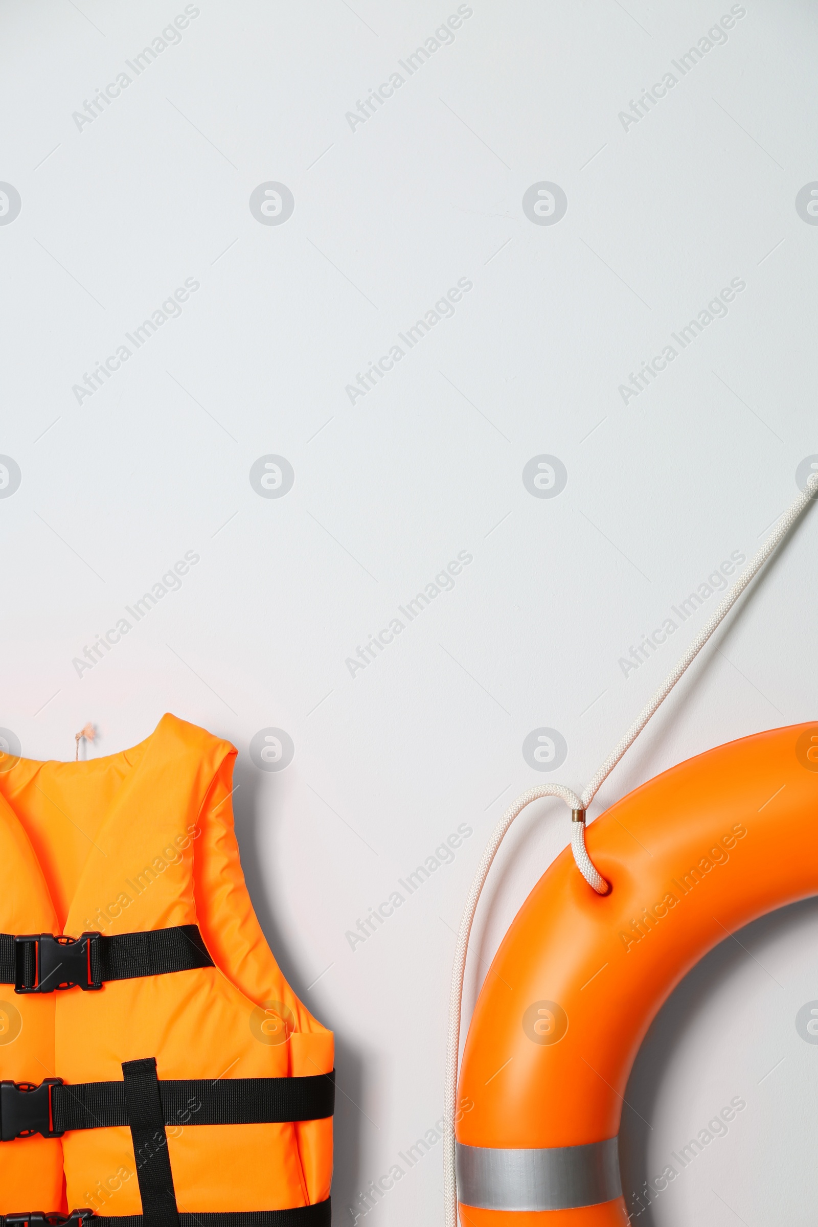 Photo of Orange life jacket, lifebuoy and space for text on light background. Rescue equipment