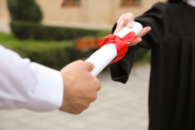 Student receiving diploma during graduation ceremony outdoors, closeup