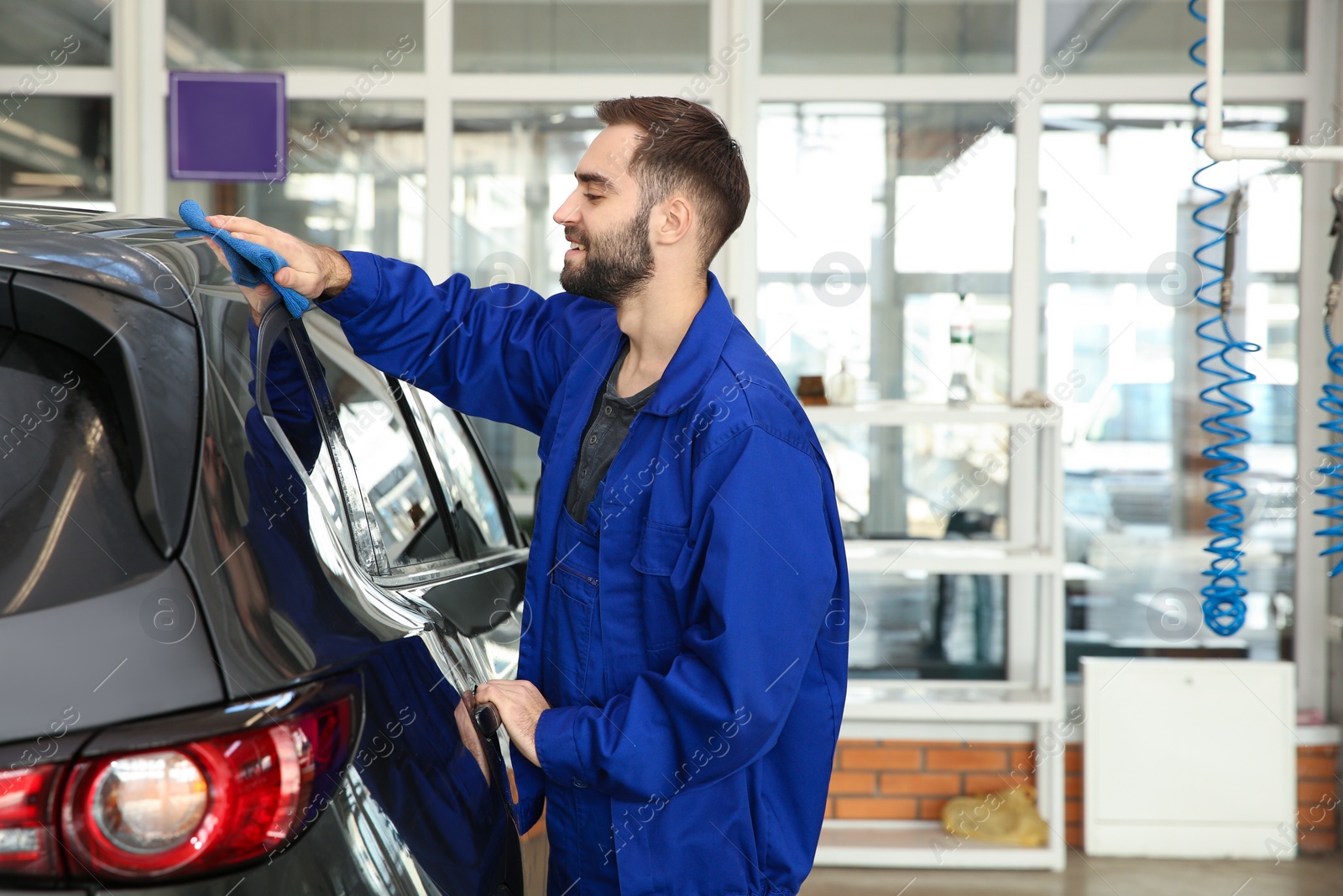 Photo of Worker cleaning automobile with rag at car wash