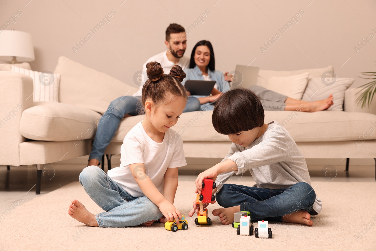 Photo of Cute children playing with toys while parents using gadgets on sofa in living room