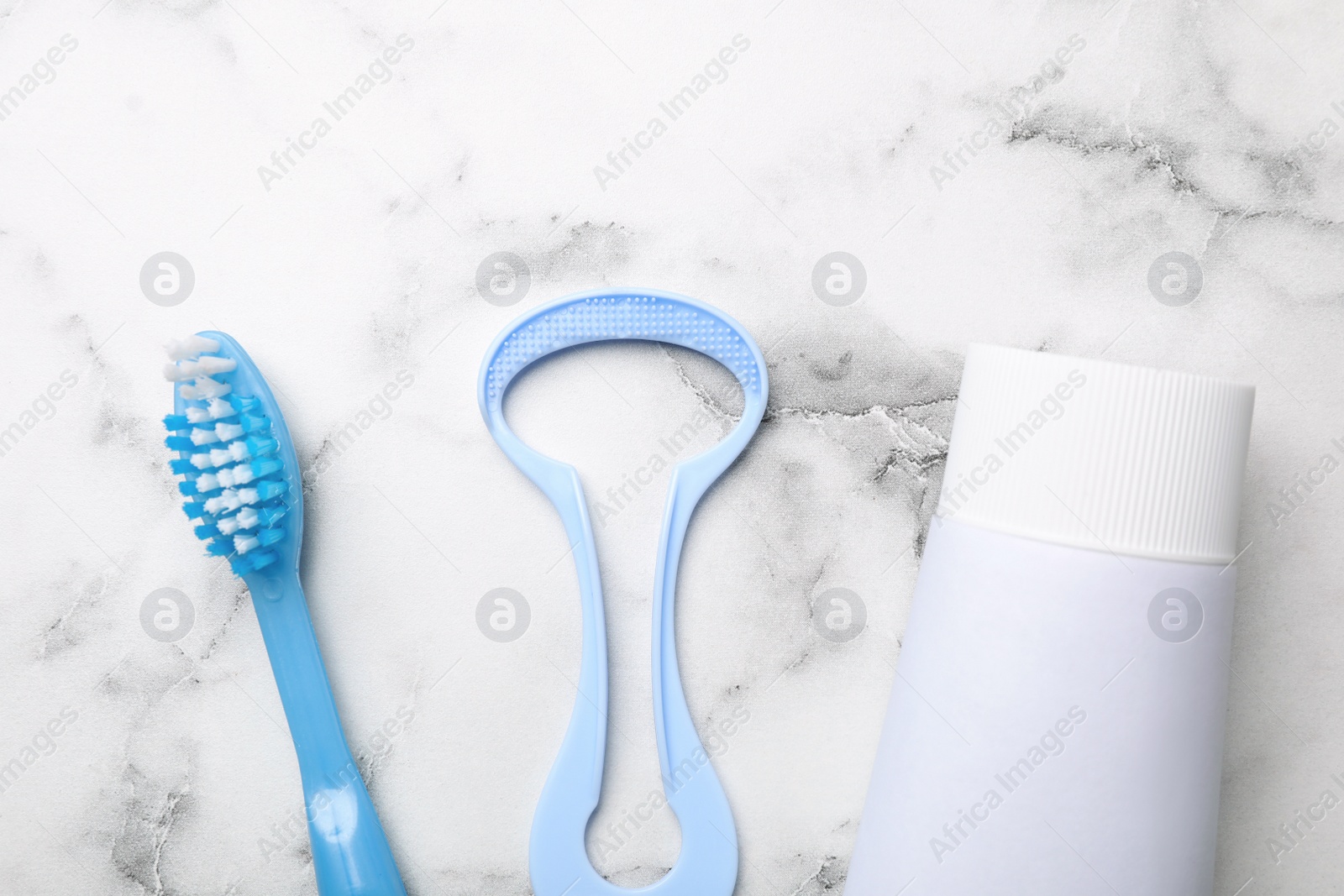 Photo of Tongue cleaner, tooth paste and brush on marble background, flat lay