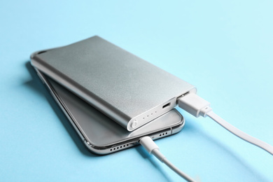 Photo of Mobile phone charging with power bank on light blue background, closeup