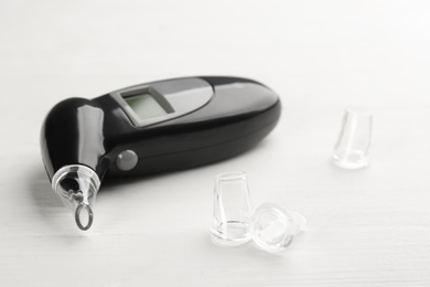 Photo of Modern breathalyzer and mouthpieces on white wooden background