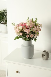 Photo of Beautiful bouquet of fresh flowers in vase on chest of drawers indoors