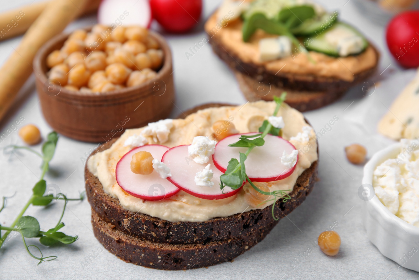 Photo of Delicious sandwiches with hummus and ingredients on light grey table, closeup