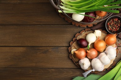 Photo of Fresh onion bulbs, leek and garlic on wooden table, flat lay. Space for text