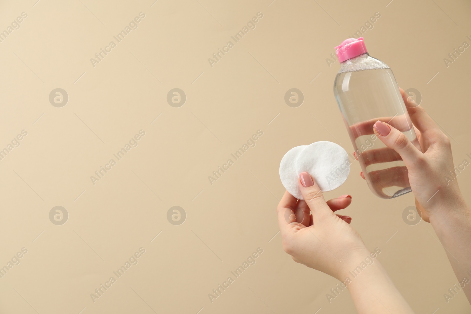 Photo of Woman holding makeup remover and cotton pads on beige background, closeup. Space for text