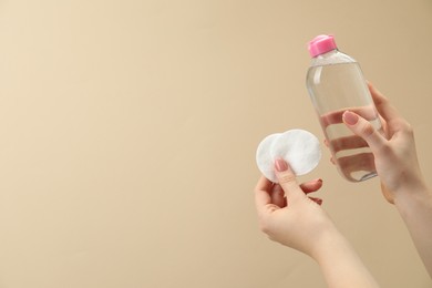 Woman holding makeup remover and cotton pads on beige background, closeup. Space for text