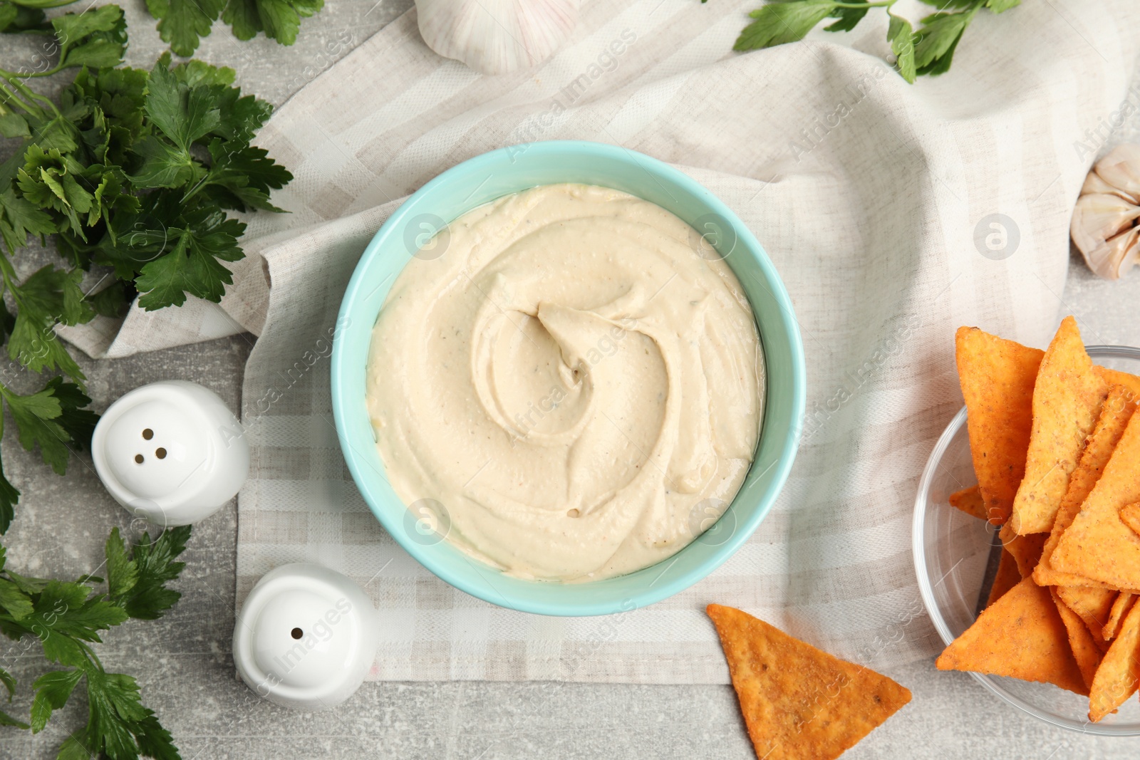 Photo of Delicious hummus, nachos and parsley on grey table, flat lay