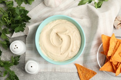 Delicious hummus, nachos and parsley on grey table, flat lay