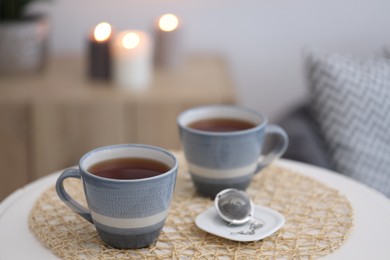 Cups of tea and snap infuser with dry leaves on white coffee table indoors, space for text