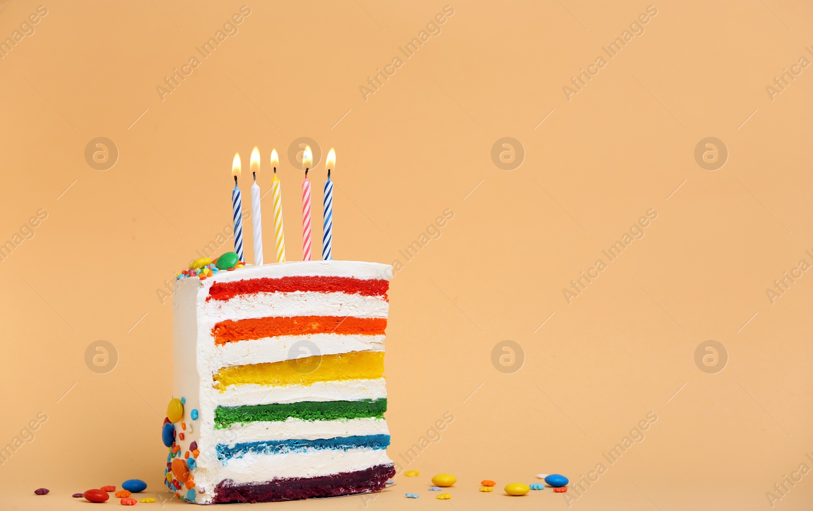 Photo of Slice of delicious rainbow cake with candles on color background