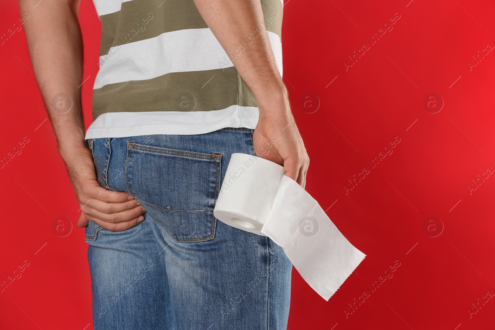 Photo of Man with toilet paper suffering from hemorrhoid on red background, closeup