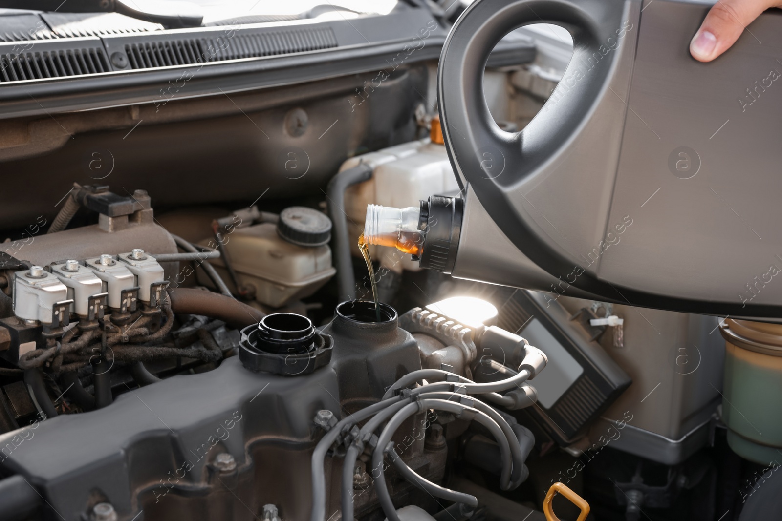 Photo of Man pouring motor oil into car engine, closeup