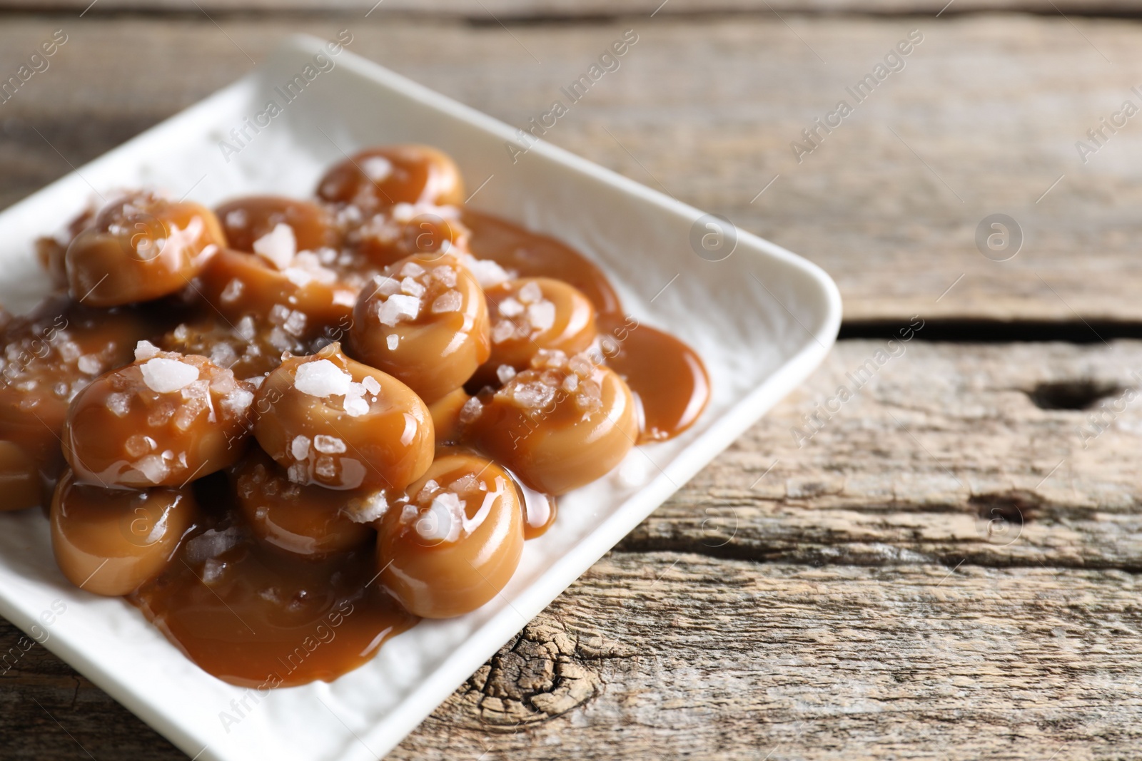 Photo of Tasty candies, caramel sauce and salt on wooden table, closeup. Space for text