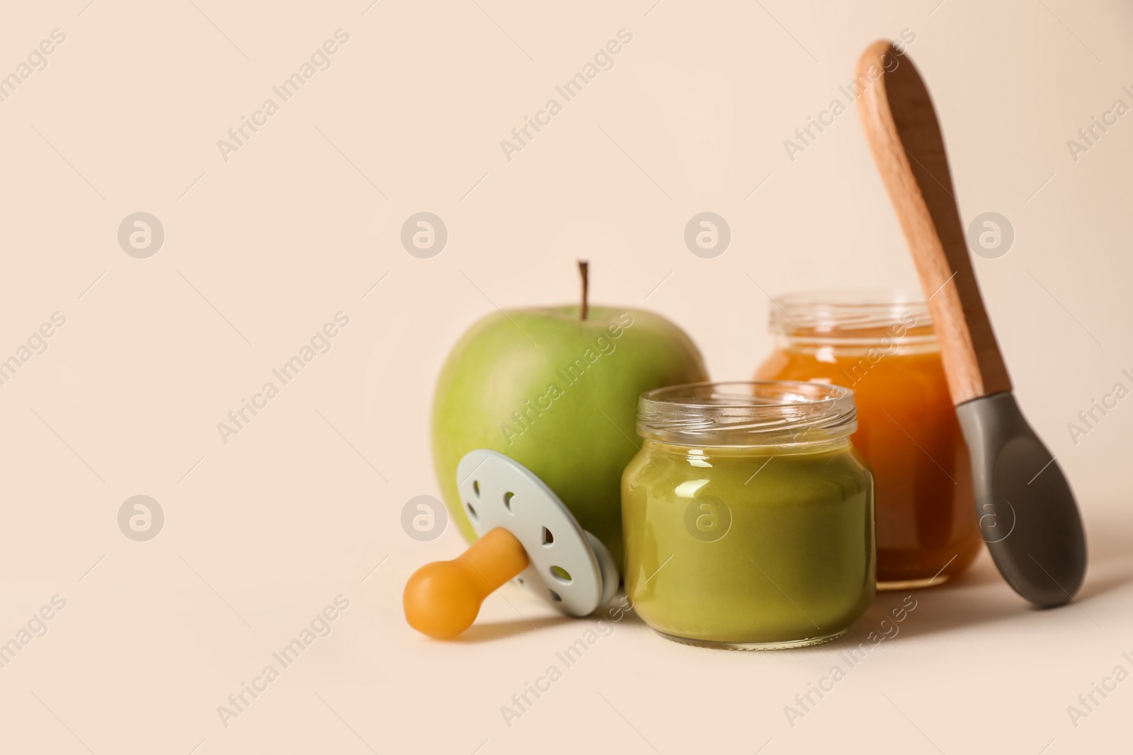 Photo of Healthy baby food, apple, pacifier and spoon on beige background. Space for text