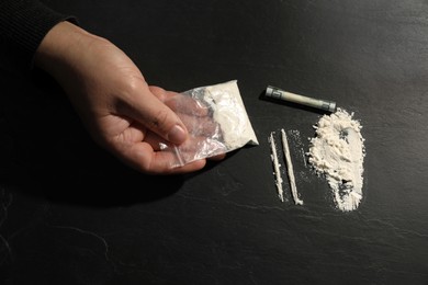 Drug addiction. Man with cocaine and rolled dollar banknote at dark textured table, top view