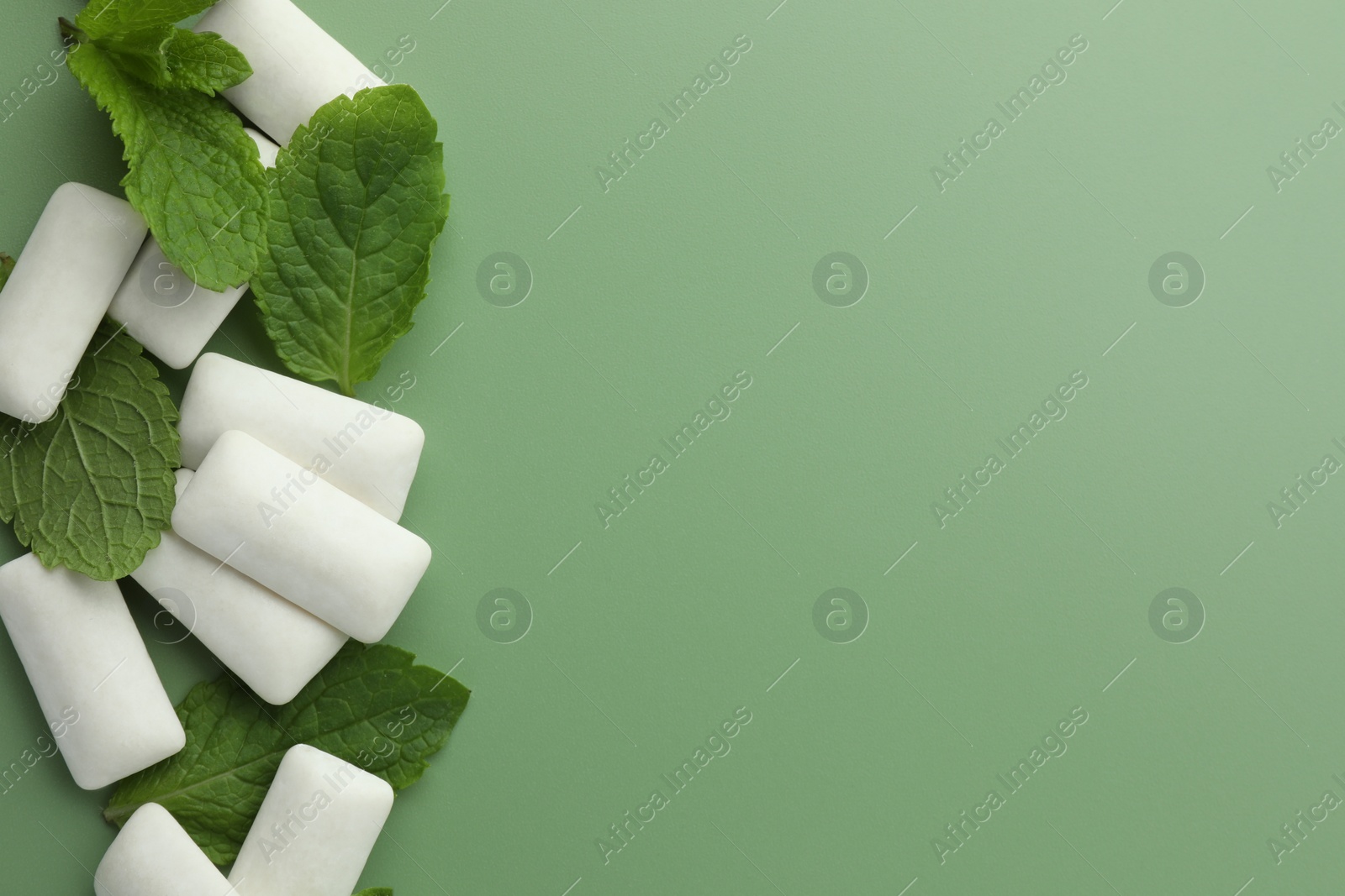 Photo of Tasty white chewing gums and mint leaves on light green background, flat lay. Space for text