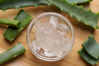 Photo of Aloe vera gel and slices of plant on wooden table, flat lay