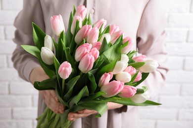 Photo of Woman holding bouquet of tulips against white brick wall, closeup
