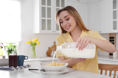 Photo of Young woman pouring milk from gallon bottle into plate with breakfast cereal at white marble table in kitchen