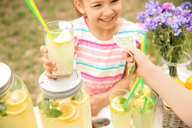 Photo of Little girl selling natural lemonade at stand in park