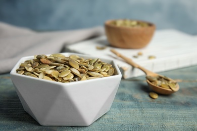 Photo of Bowl of raw pumpkin seeds on blue wooden table, closeup. Space for text