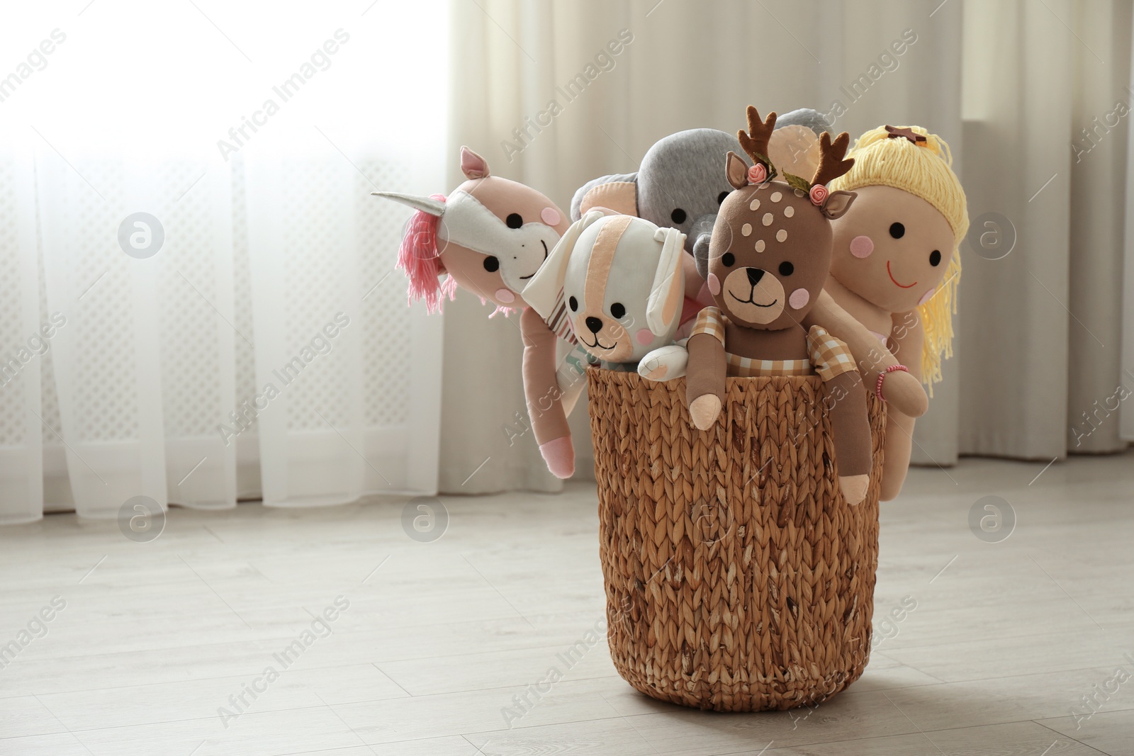 Photo of Funny stuffed toys in basket on floor, space for text. Children's room interior decor