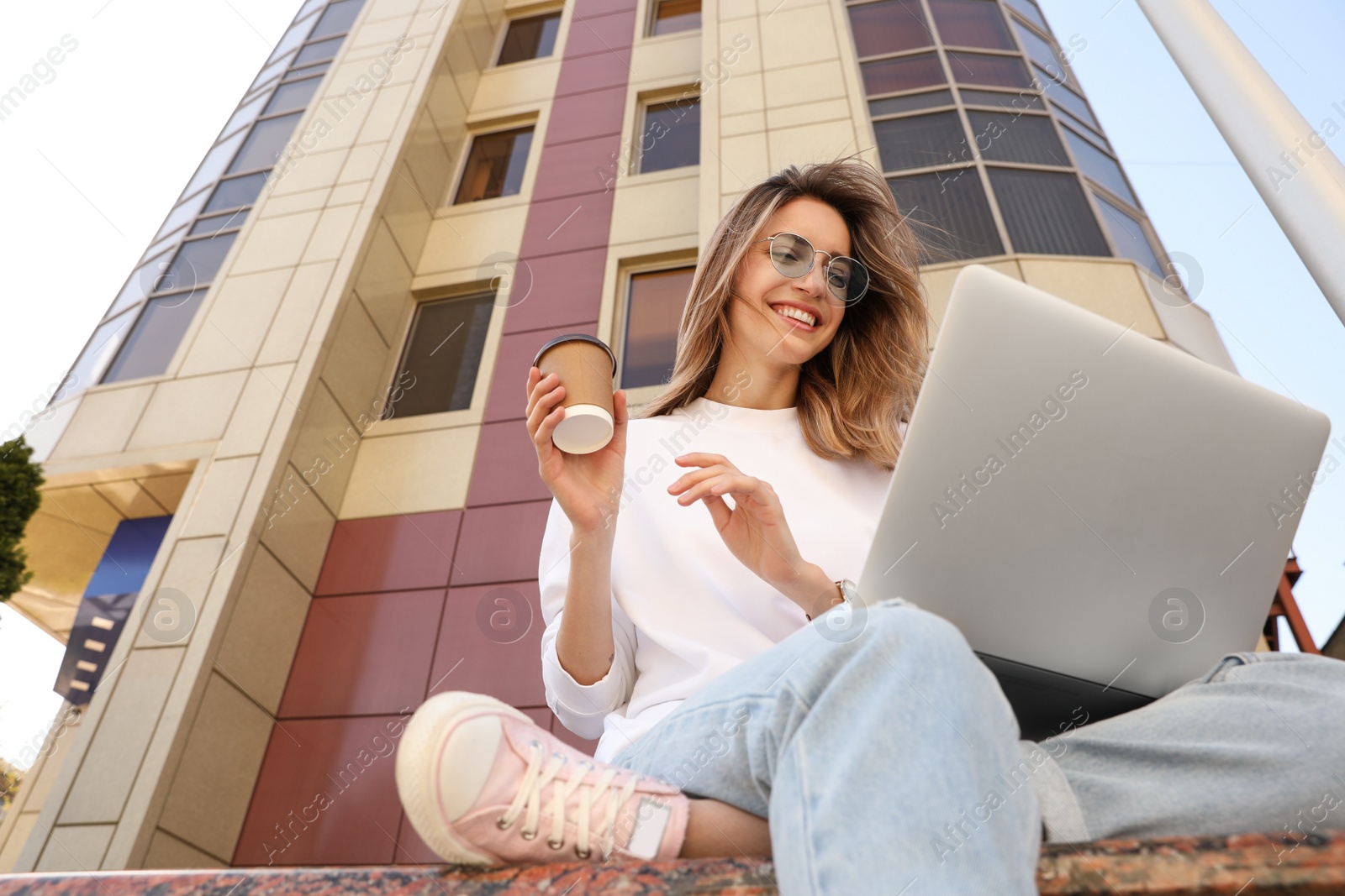 Image of Young woman with paper cup of coffee and laptop outdoors