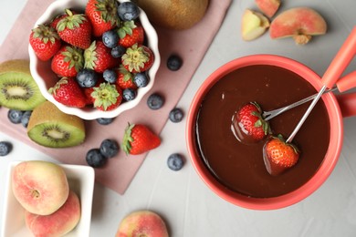 Photo of Dipping strawberries into fondue pot with chocolate on grey table, top view