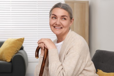 Photo of Senior woman with walking cane sitting on armchair at home