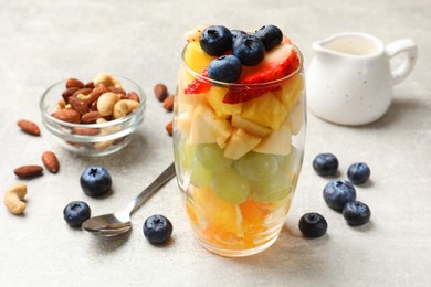 Delicious fruit salad, fresh berries and nuts on light grey table