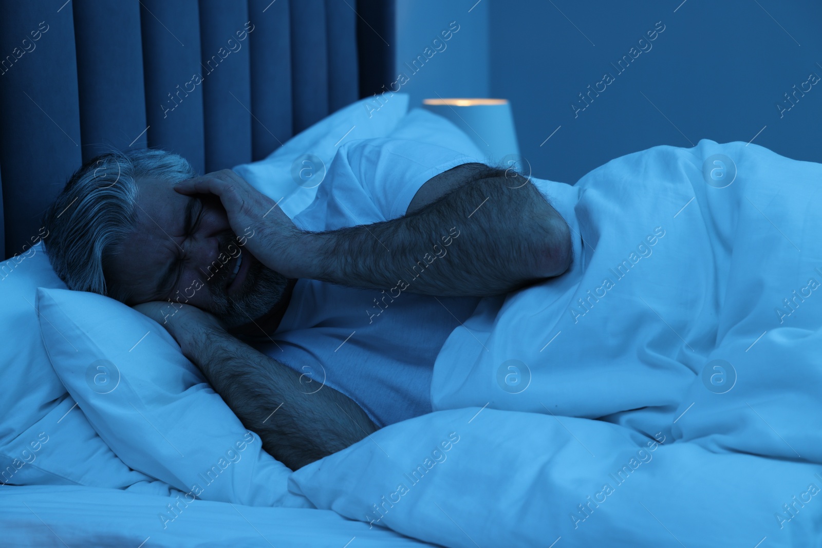 Photo of Mature man suffering from headache in bed at night