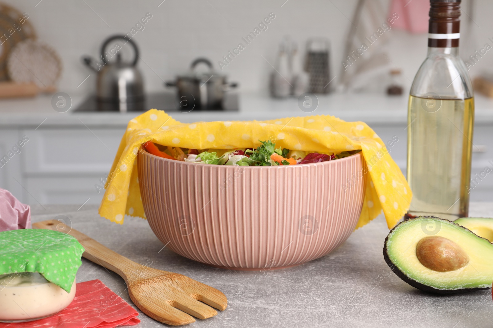 Photo of Bowl of fresh salad covered with beeswax food wrap on light grey table in kitchen