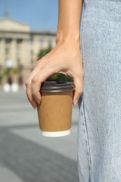 Photo of Woman holding takeaway cardboard coffee cup with plastic lid outdoors, closeup