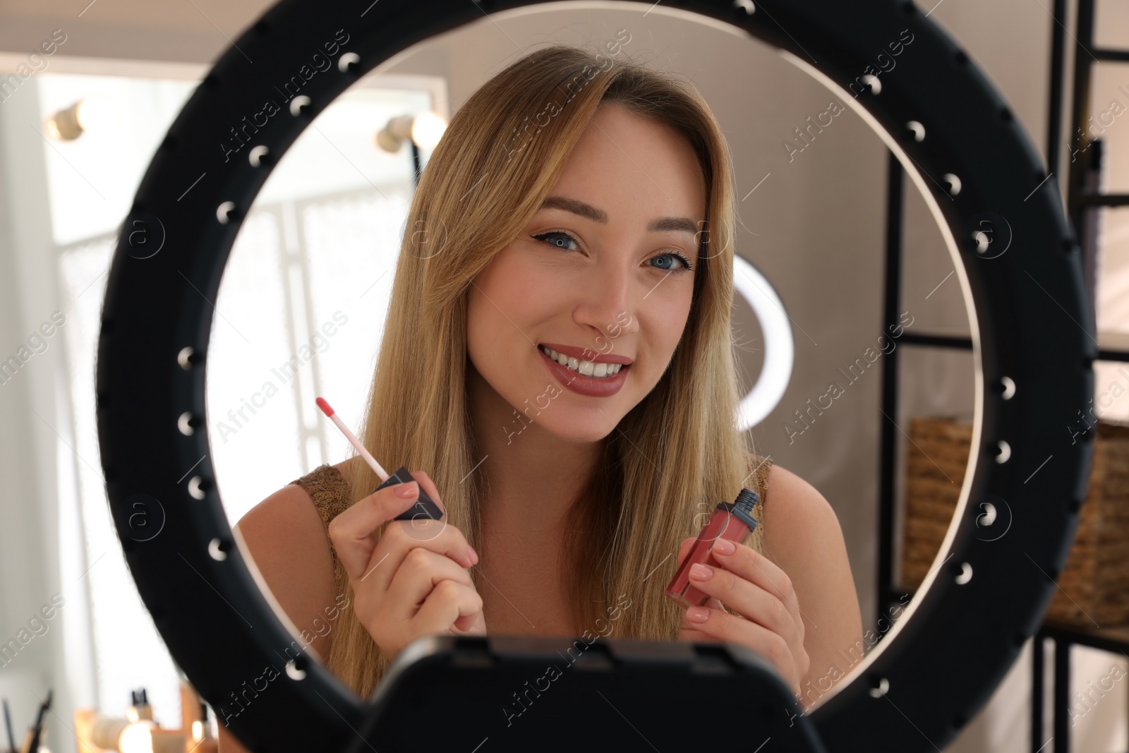 Photo of Beautiful young woman with liquid lipstick indoors, view through ring lamp