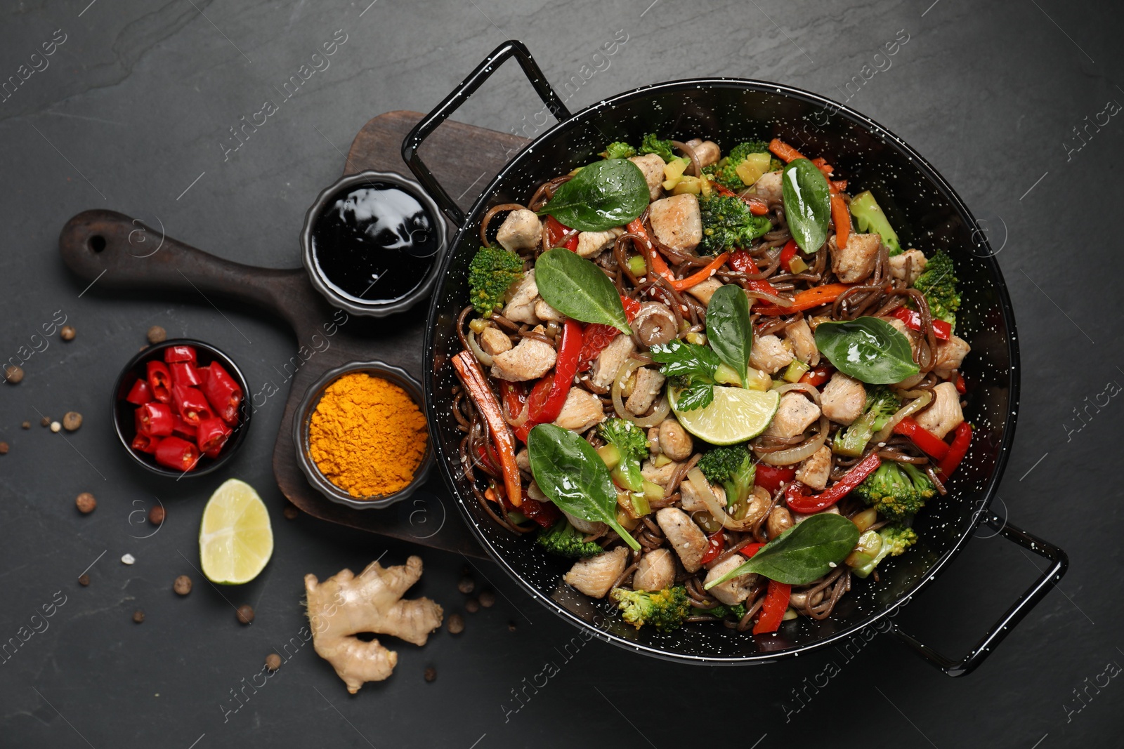 Photo of Stir-fry. Tasty noodles with meat in wok and ingredients on grey textured table, flat lay