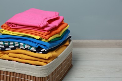 Photo of Laundry basket with clean stacked clothes on floor near grey wall, closeup. Space for text
