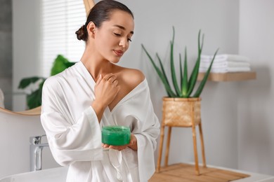 Young woman applying aloe gel onto her skin in bathroom. Space for text