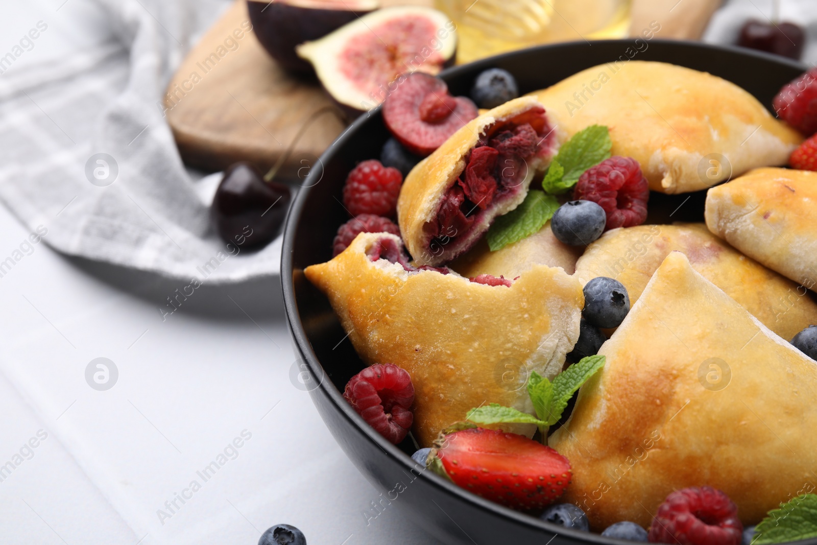 Photo of Bowl with delicious samosas, berries and mint leaves on white tiled table, closeup. Space for text