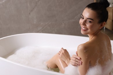 Woman taking bath with shower gel indoors