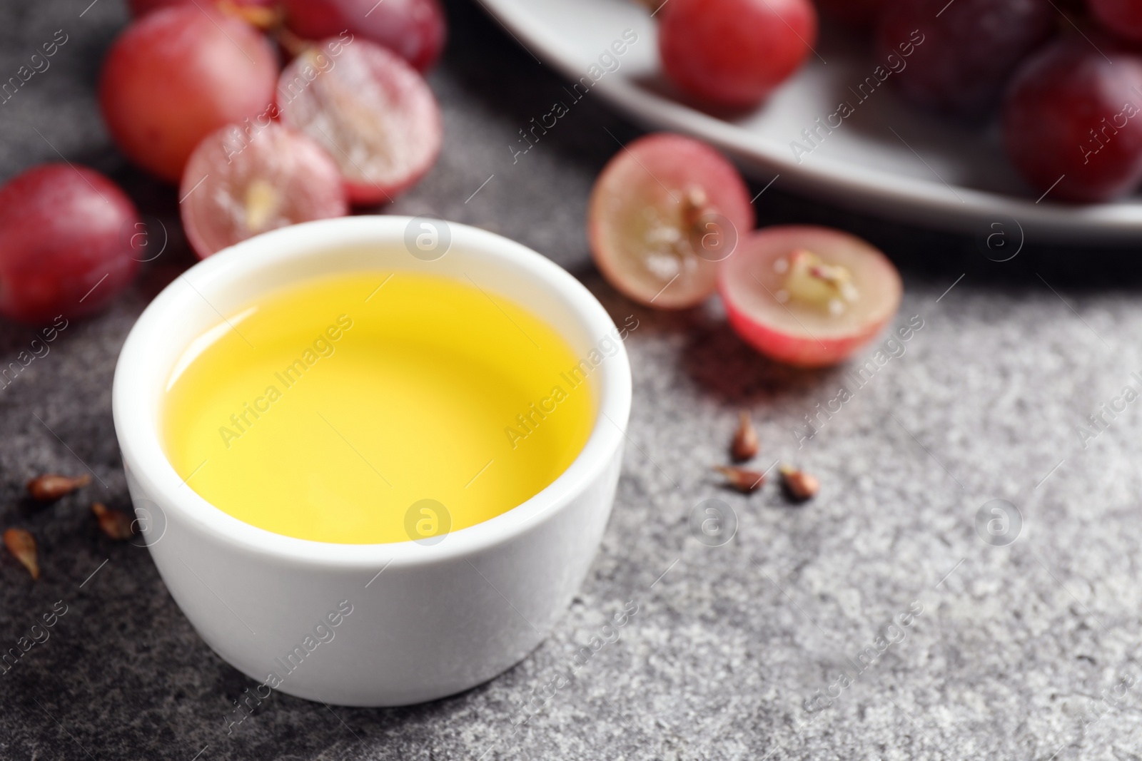 Photo of Bowl of natural grape seed oil on grey table. Organic cosmetic