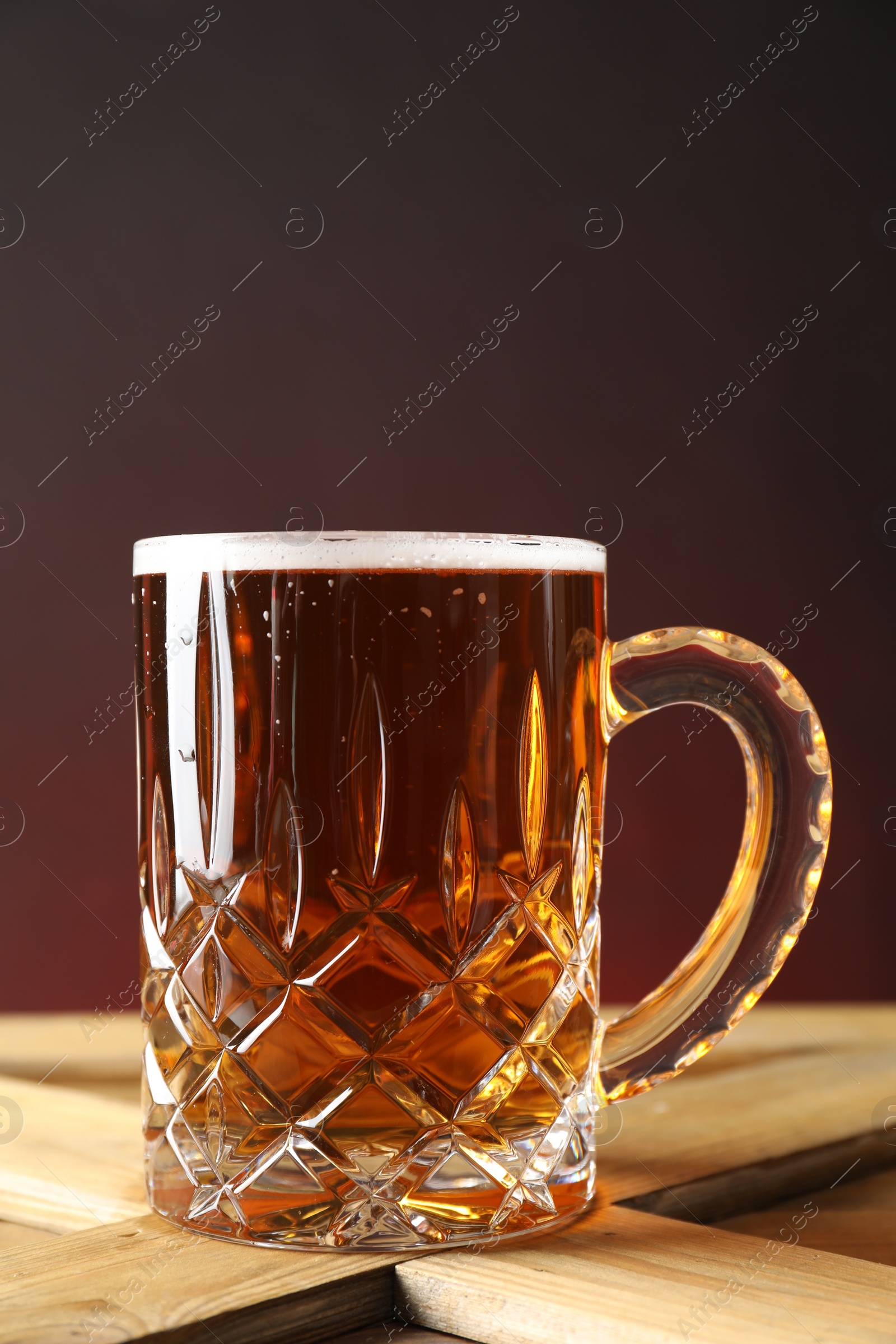 Photo of Mug with fresh beer on wooden crate against color background