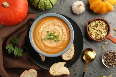 Flat lay composition with bowl of delicious pumpkin soup on grey textured table