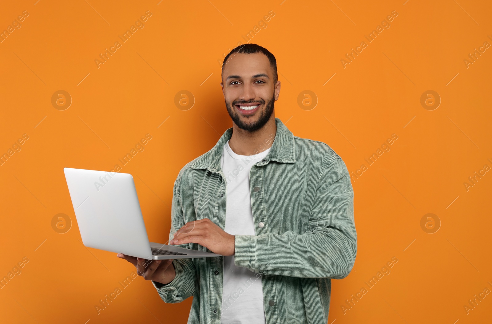 Photo of Smiling young man working with laptop on orange background